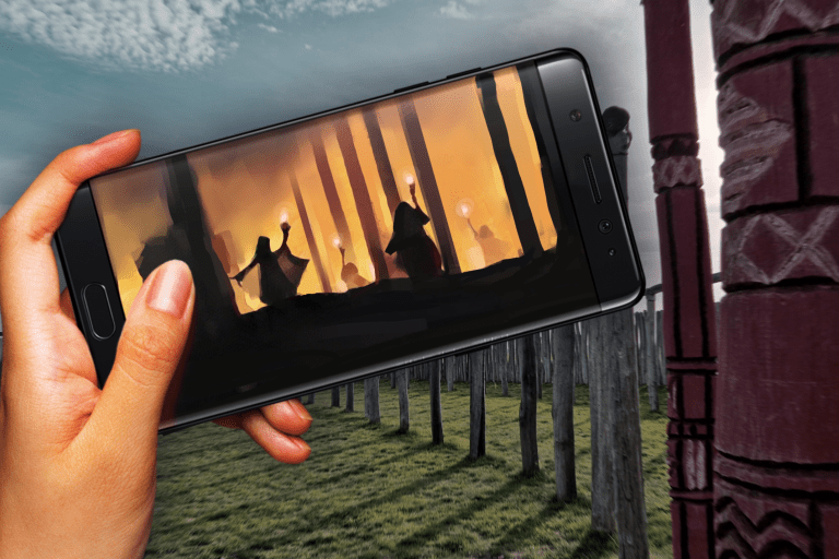 Hand met een telefoon met daarop een monument van palen